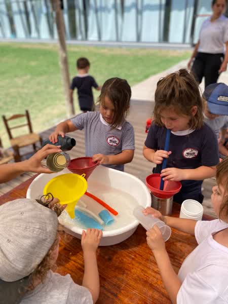 Chicos explorando con utensilios y agua alrededor de una palangana